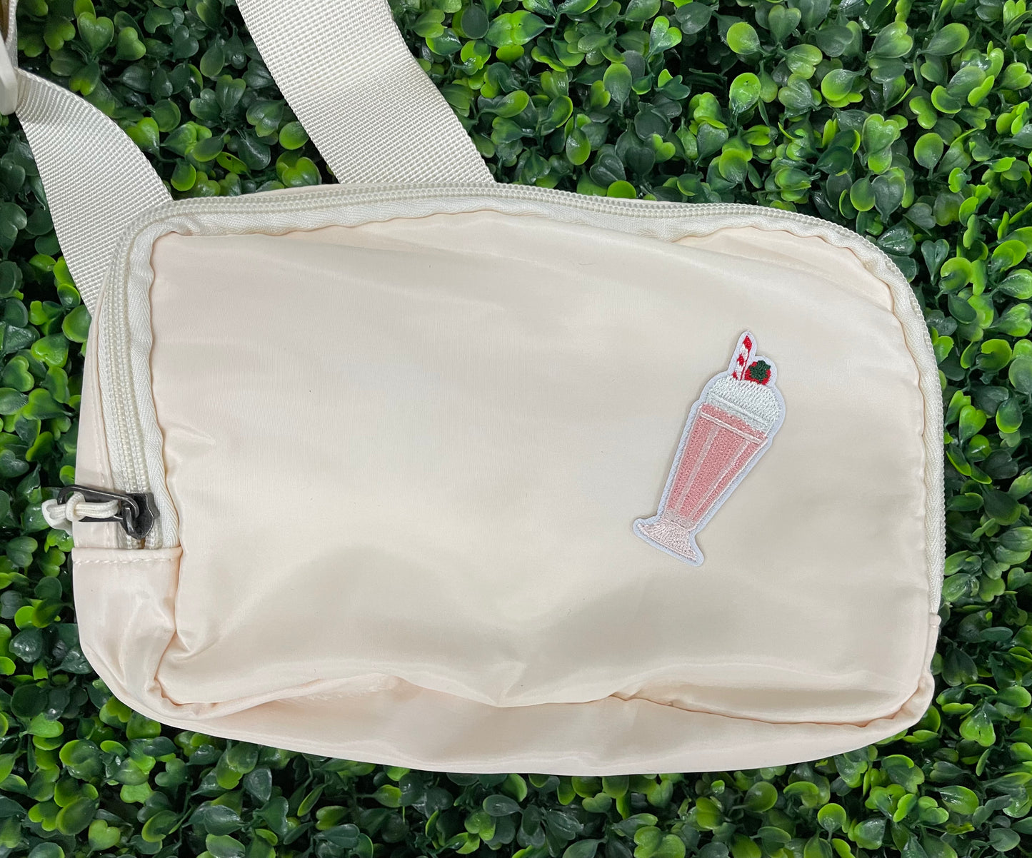 A pink milkshake embroidered patch with a cherry on top, held onto a white shoulder bag