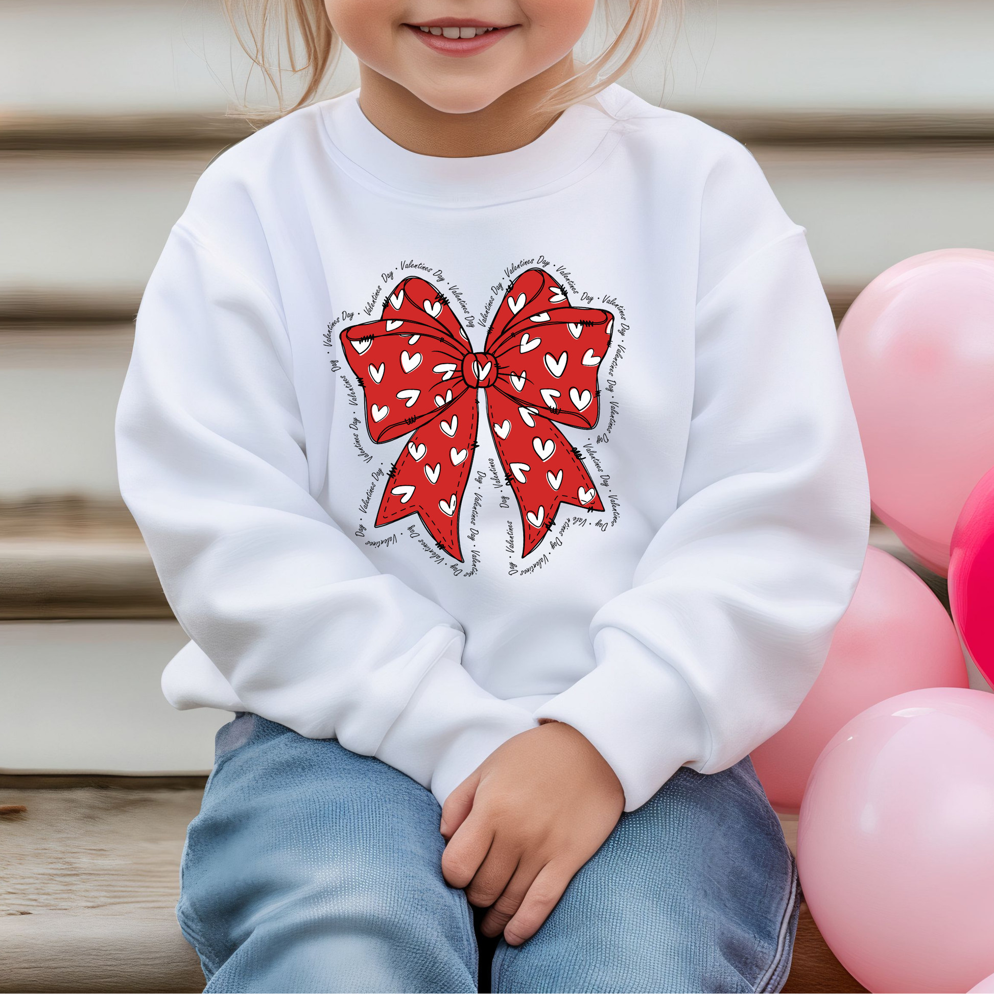 Front view of a kids sweatshirt with a Red bow with white hearts with Valentines Day written all around it. 
