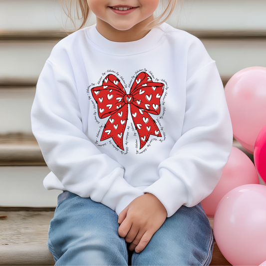 Front view of a kids sweatshirt with a Red bow with white hearts with Valentines Day written all around it. 