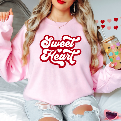 Front view of a pink sweatshirt with Red letters spelling out Sweet Heart on it. The backdrop is a girl holding a coffee. 