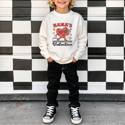 A child standing in front of a checkered background wearing a white sweatshirt with 'Mama's Valentine' text and a heart graphic character on it.