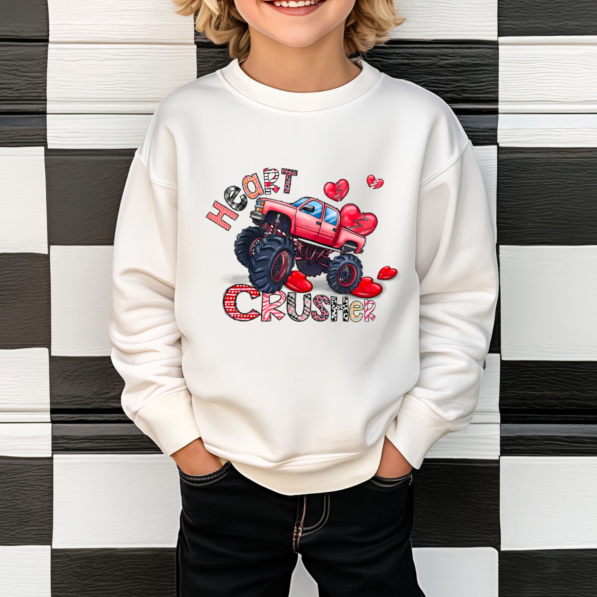 A child wearing a white sweatshirt with a red and gray monster truck design and the text 'HEART CRUSHER' on the front, standing against a checkered background.