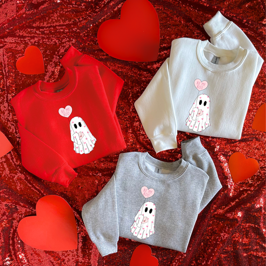 Three kids' sweatshirts in red, gray, and white, each featuring a heart-shaped balloon with the phrase 'BE MY BOO'. The sweatshirts are presented on a red glittery background with real red hearts around.