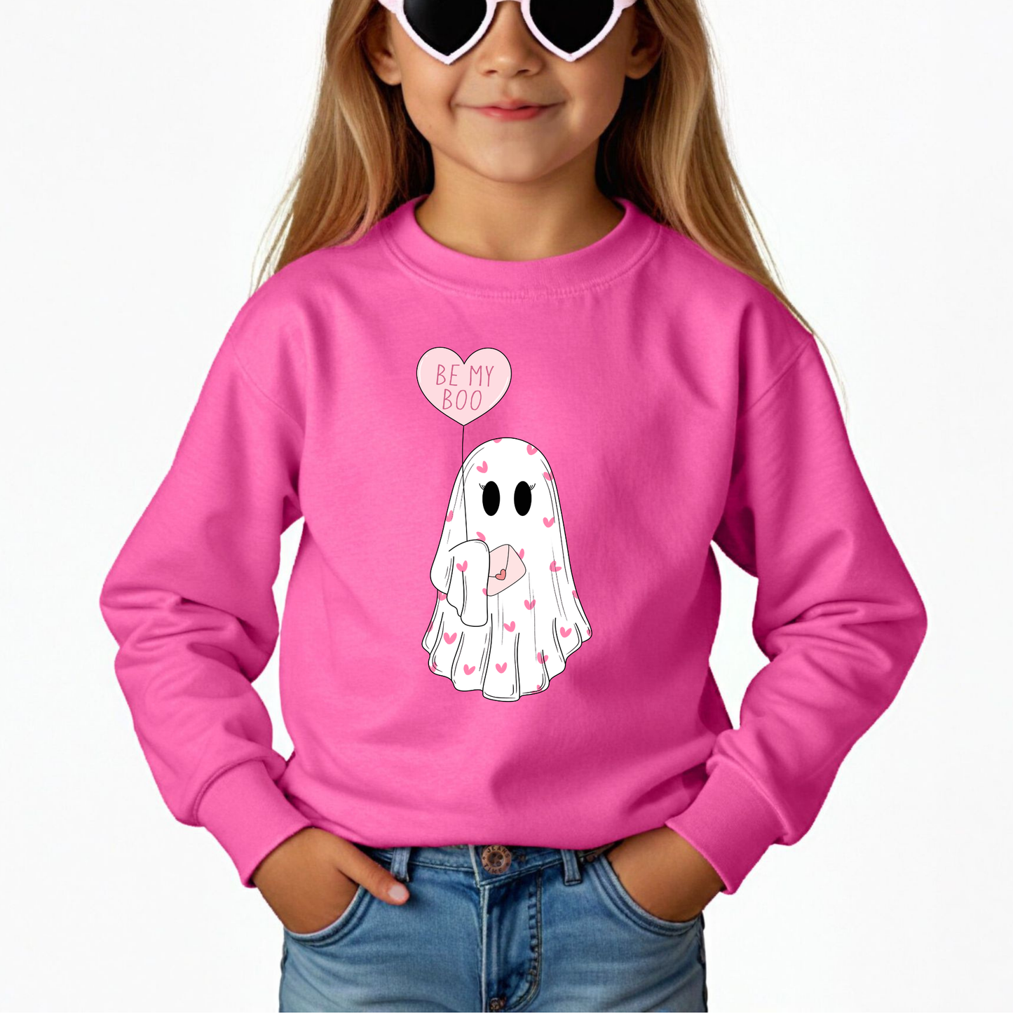 A child wearing a sweatshirt in hot pink,  featuring a heart-shaped balloon with the phrase 'BE MY BOO'. 