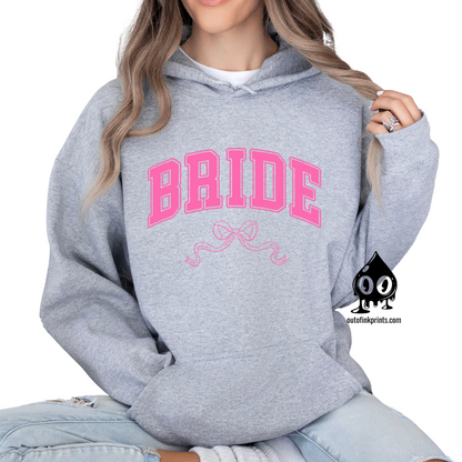 A woman wearing a gray hoodie with the word 'Bride' and a pink bow printed on the front.