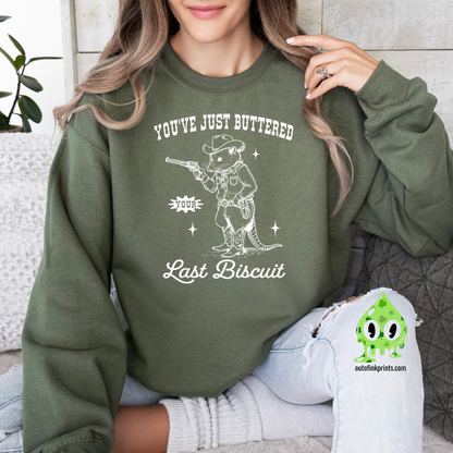 A person wearing a dark green sweatshirt with the text 'You've Just Buttered Last Biscuit' and an illustration of a mouse holding a gun.