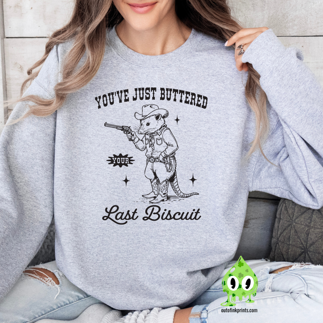 A person wearing a gray sweatshirt with the text 'You've Just Buttered Last Biscuit' and an illustration of a mouse holding a gun.