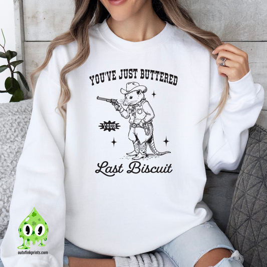 A person wearing a white sweatshirt with the text 'You've Just Buttered Last Biscuit' and an illustration of a mouse holding a gun.