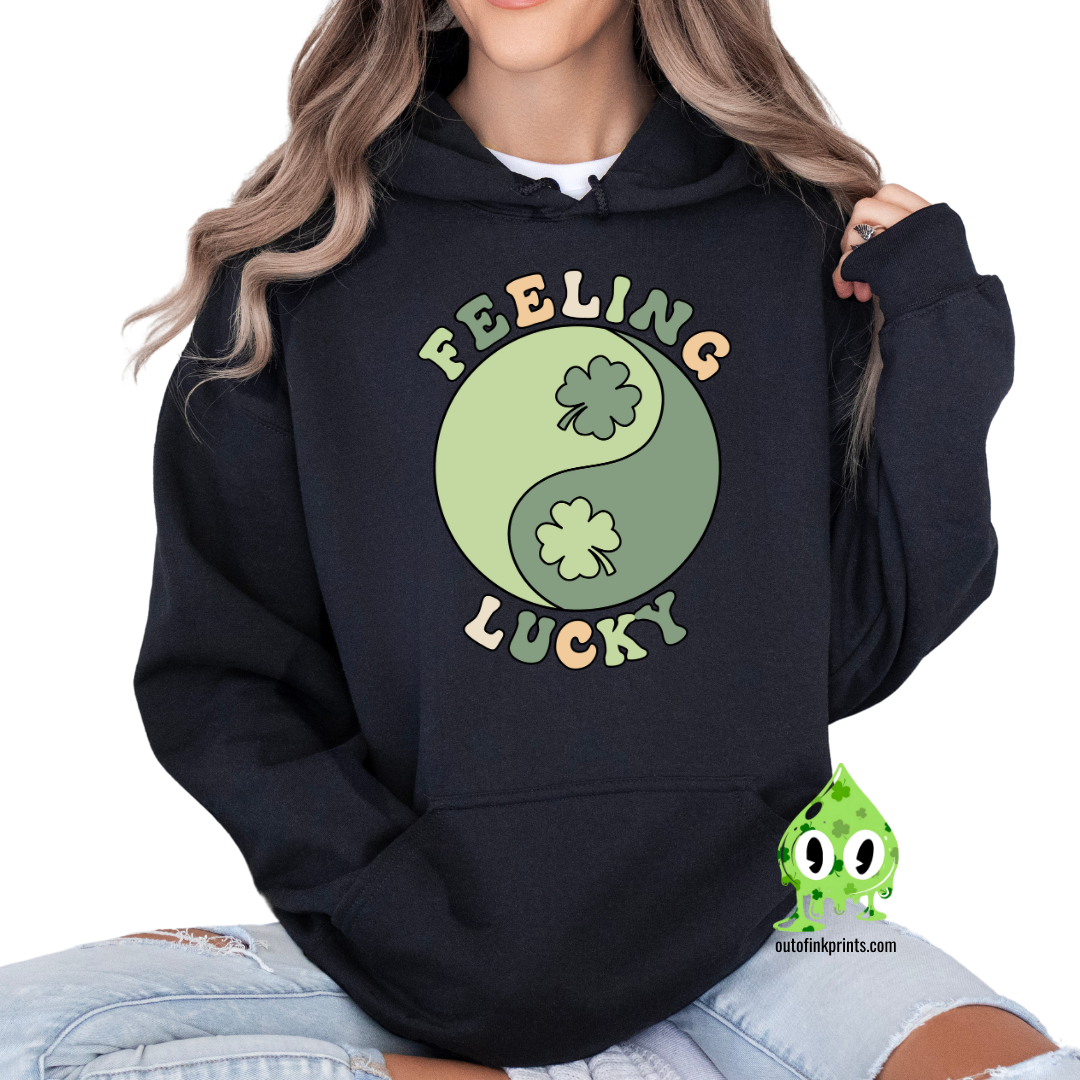 A black hoodie with the text 'FEELING LUCKY' and a graphic of a yin-yang symbol with clovers on both sides.