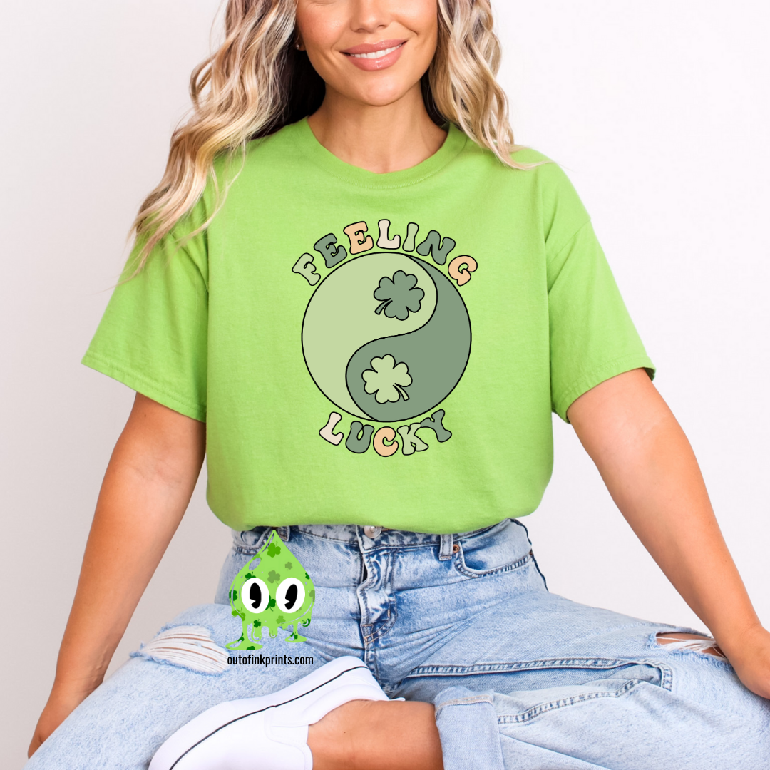 A green t-shirt with 'Feeling Lucky Yin & Yang' text and shamrock graphics, paired with blue denim jeans.