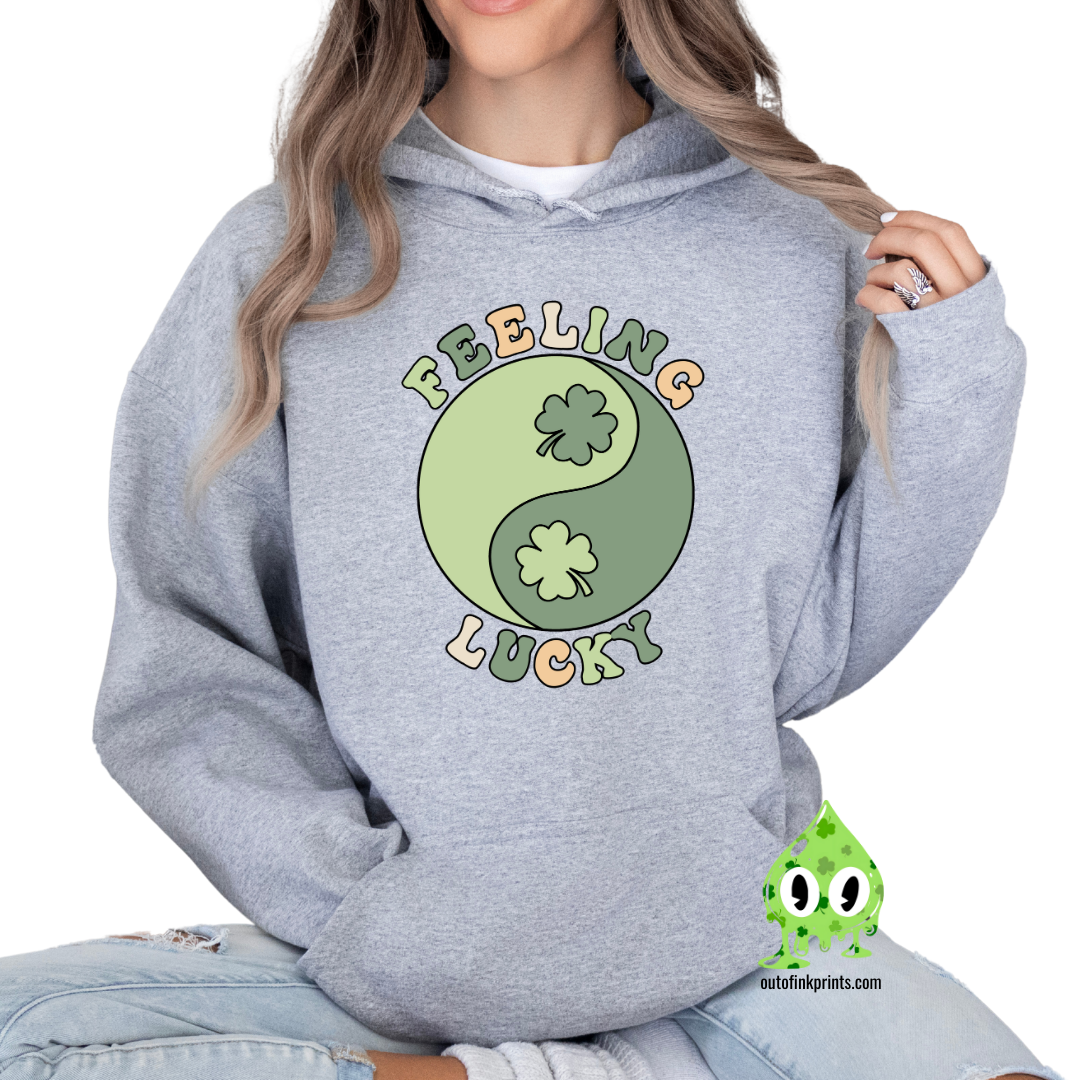 A gray hoodie with the text 'FEELING LUCKY' and a graphic of a yin-yang symbol with clovers on both sides.