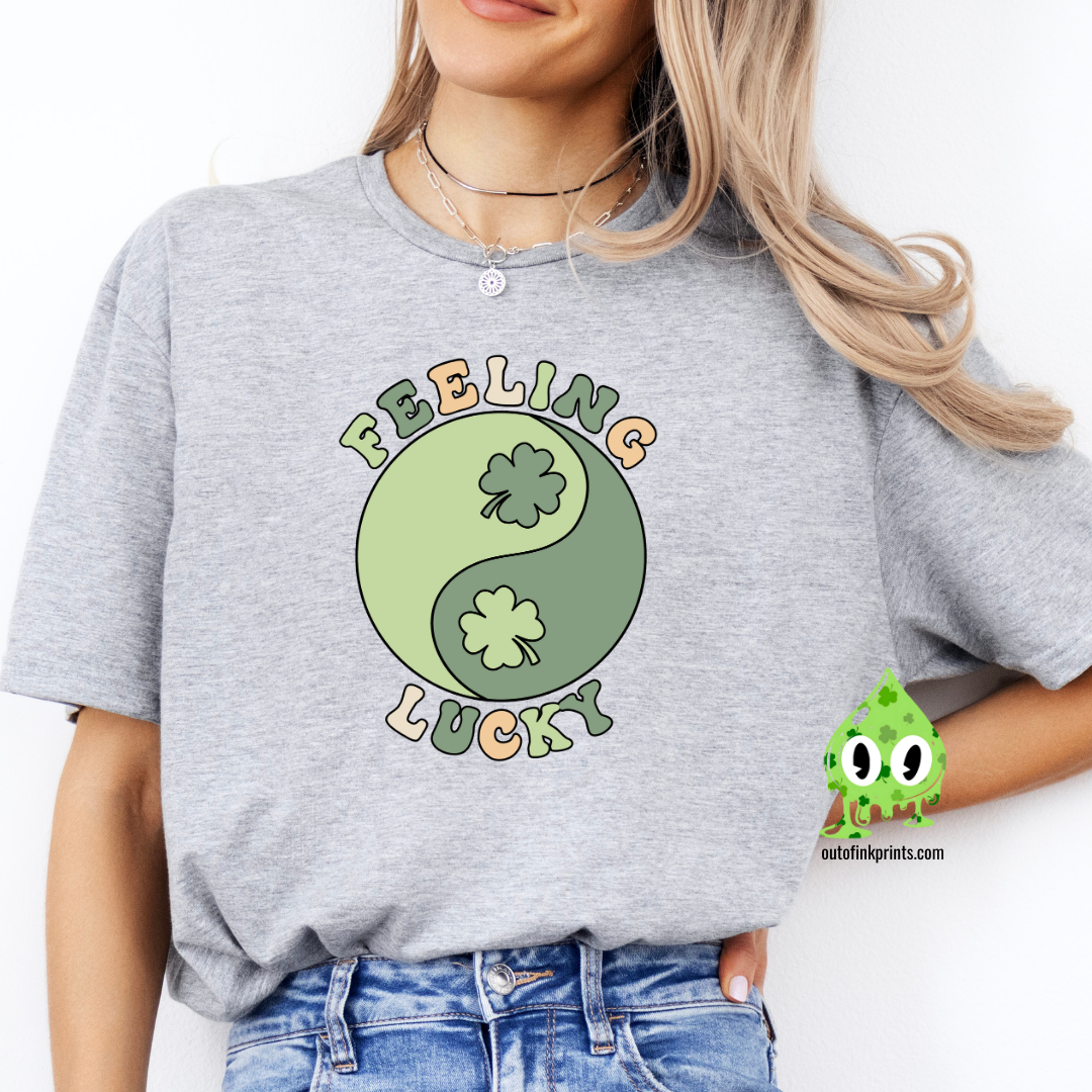 A woman wearing a gray t-shirt with 'Feeling Lucky Yin & Yang' text and shamrock graphics, paired with blue denim jeans.
