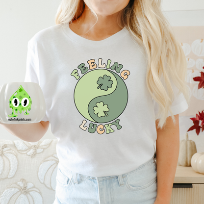 A woman wearing a white t-shirt with 'Feeling Lucky Yin & Yang' text and shamrock graphics, paired with blue denim jeans.