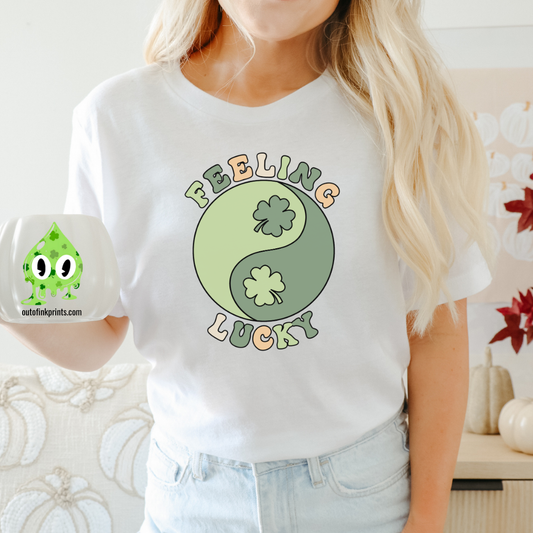 A woman wearing a white t-shirt with 'Feeling Lucky Yin & Yang' text and shamrock graphics, paired with blue denim jeans.
