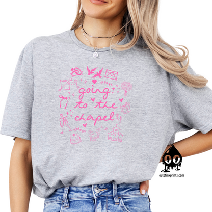 A person wearing a gray T-shirt with pink text and graphics related to a bride and chapel