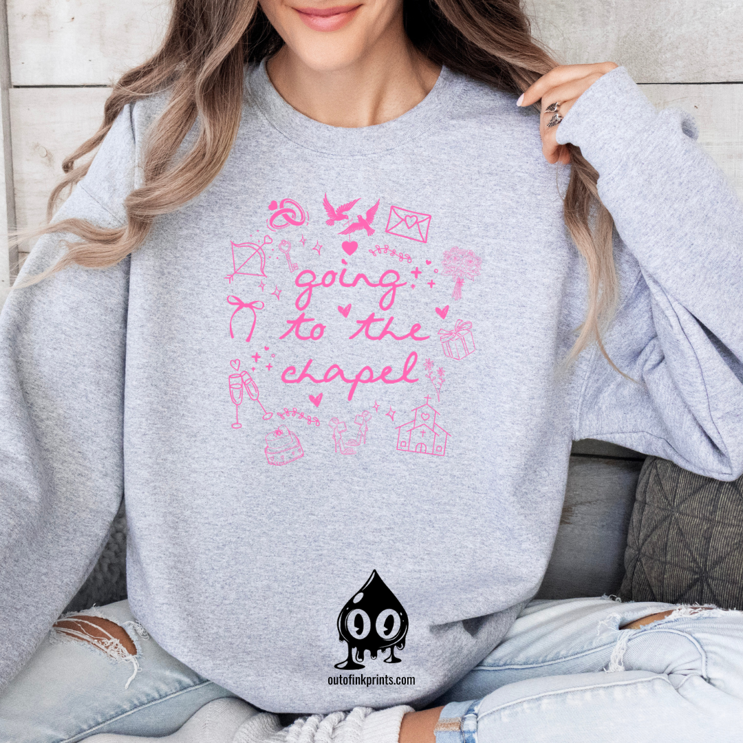 A woman sitting and wearing a gray sweatshirt with pink text that reads 'Going to the Chapel' along with various symbols and text related to weddings.