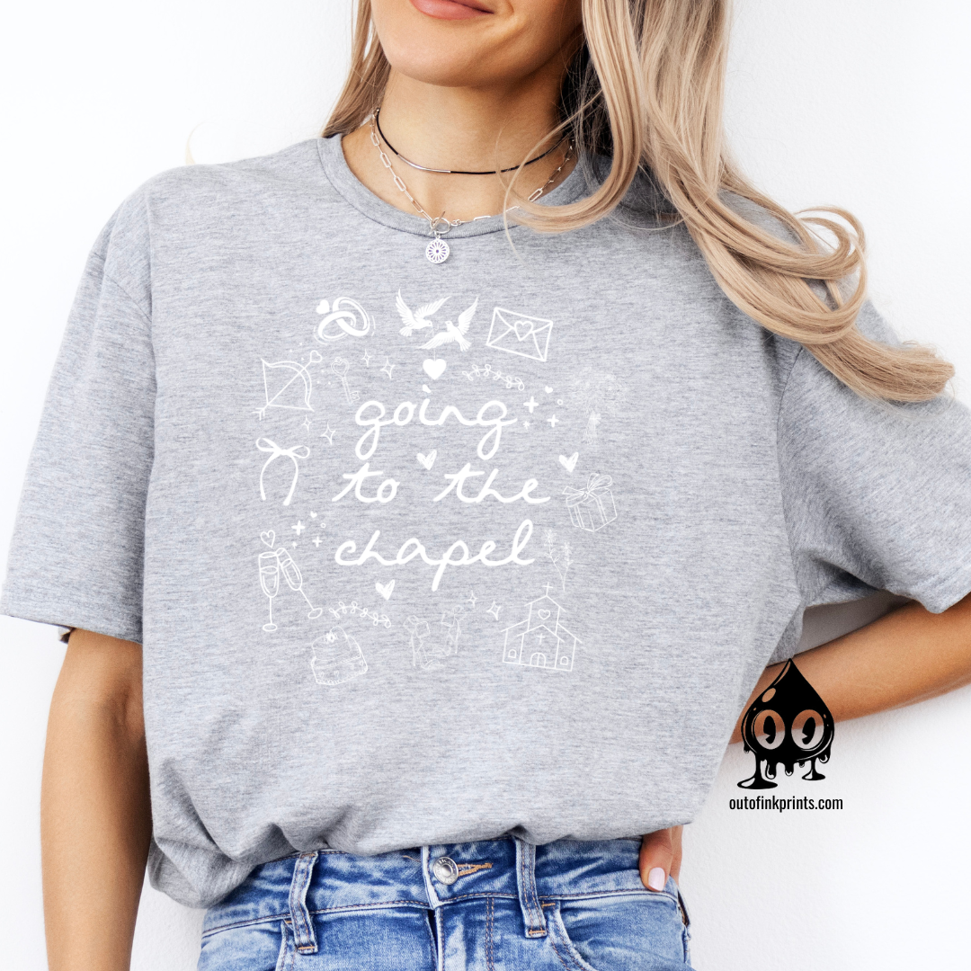 A woman wearing a gray T-shirt with white text that reads 'Going to the Chapel' along with various symbols and text related to weddings.