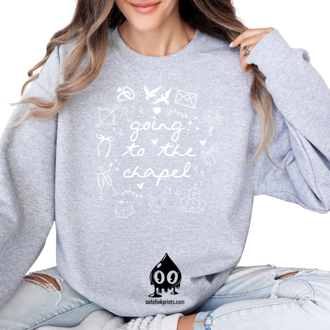 A woman sitting wearing a gray sweatshirt with white text that reads 'GOING TO THE CHAPEL' and various illustrations such as a bride, groom, and wedding-related icons.