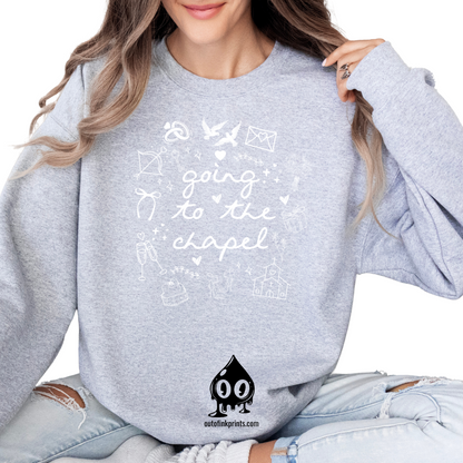 A woman sitting wearing a gray sweatshirt with white text that reads 'GOING TO THE CHAPEL' and various illustrations such as a bride, groom, and wedding-related icons.