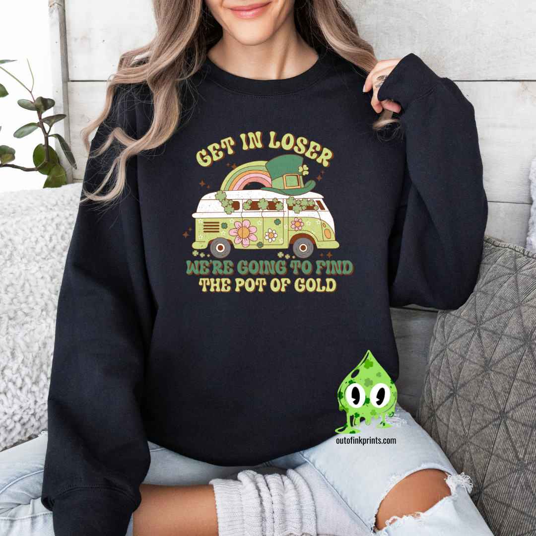 A woman wearing a black sweatshirt with a St. Patrick's Day theme, featuring text and a graphic of a rainbow, clover, and what appears to be a leprechaun.