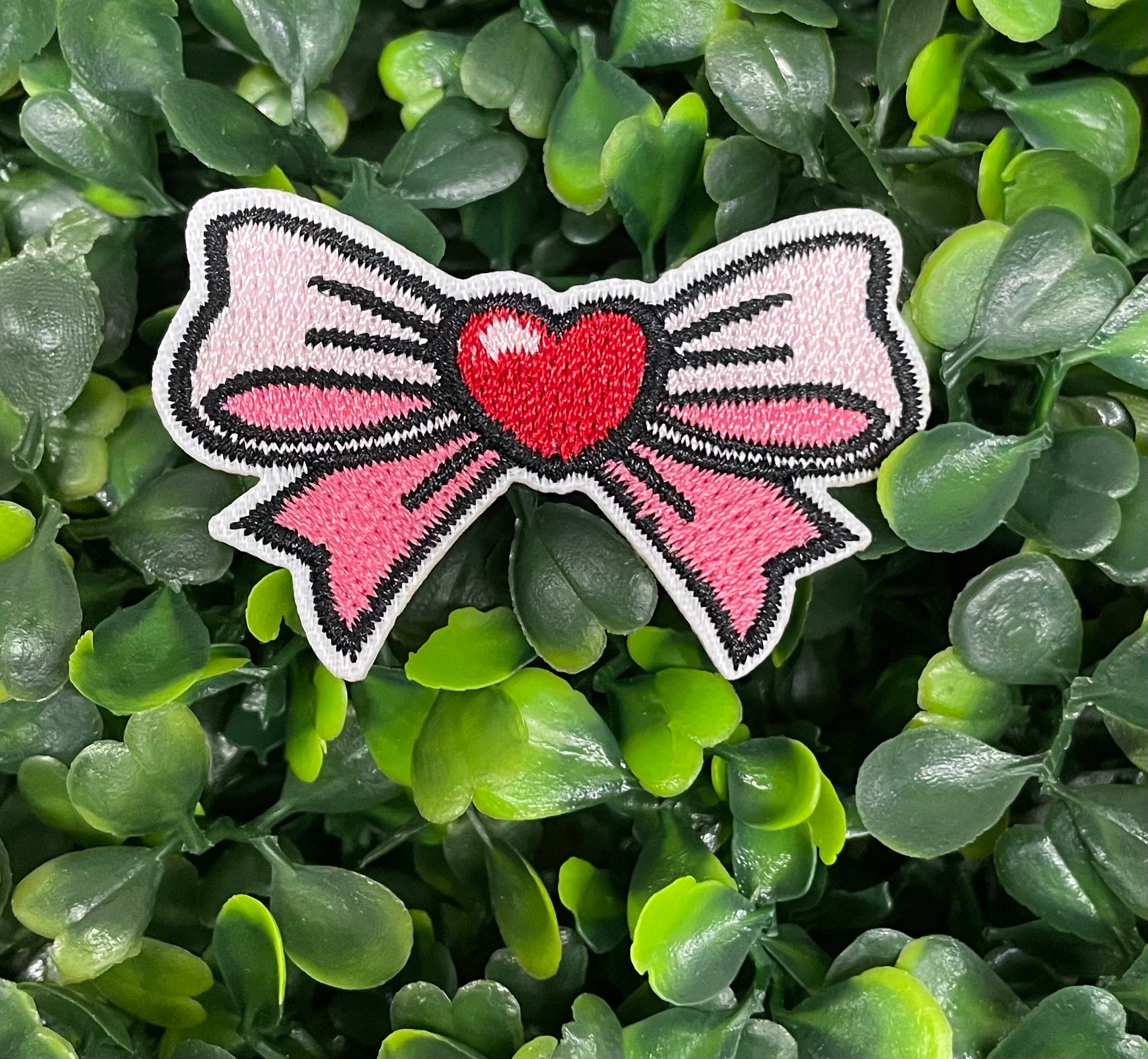 A patch with a pink and white bow design and a heart in the center