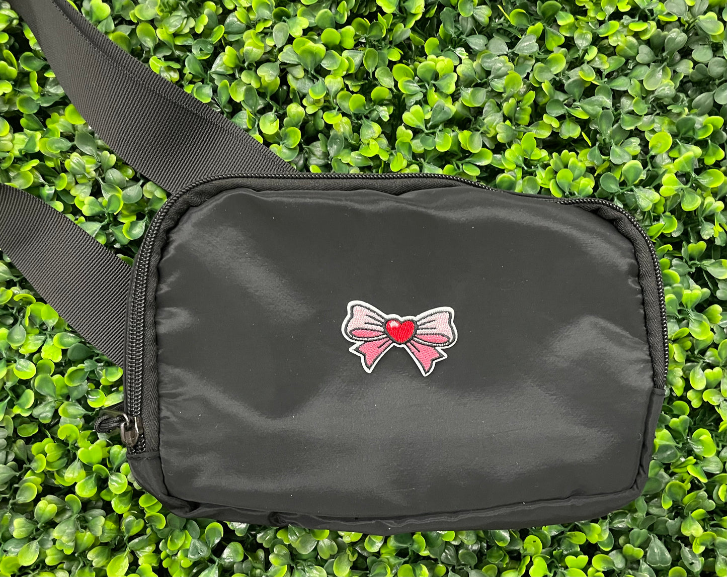 An black bag that has a patch with a pink and white bowtie design and a heart in the center