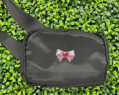 An black bag that has a patch with a pink and white bowtie design and a heart in the center