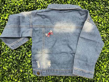 Blue jean jacket with a patch attached to the back that has a pink and white bowtie design with a heart in the center