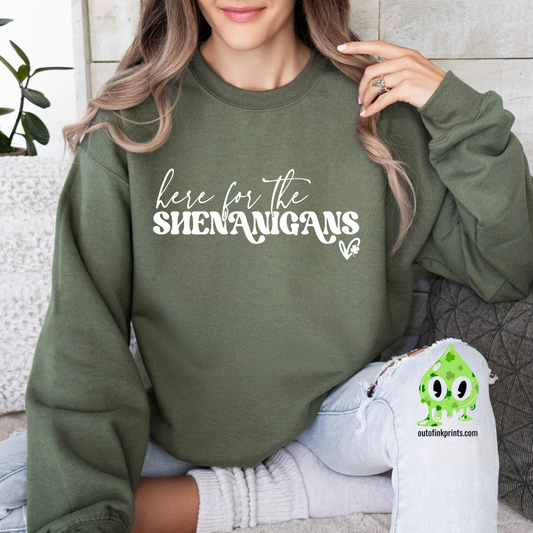 A woman wearing a green sweatshirt with the text 'here for the SHENANIGANS' printed on it.