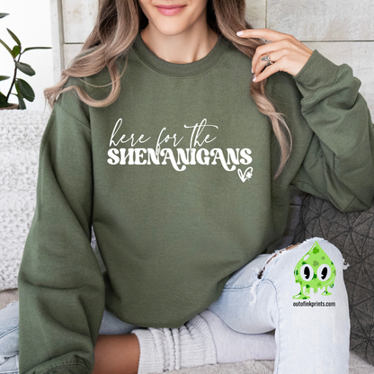 A woman wearing a green sweatshirt with the text 'here for the SHENANIGANS' printed on it.