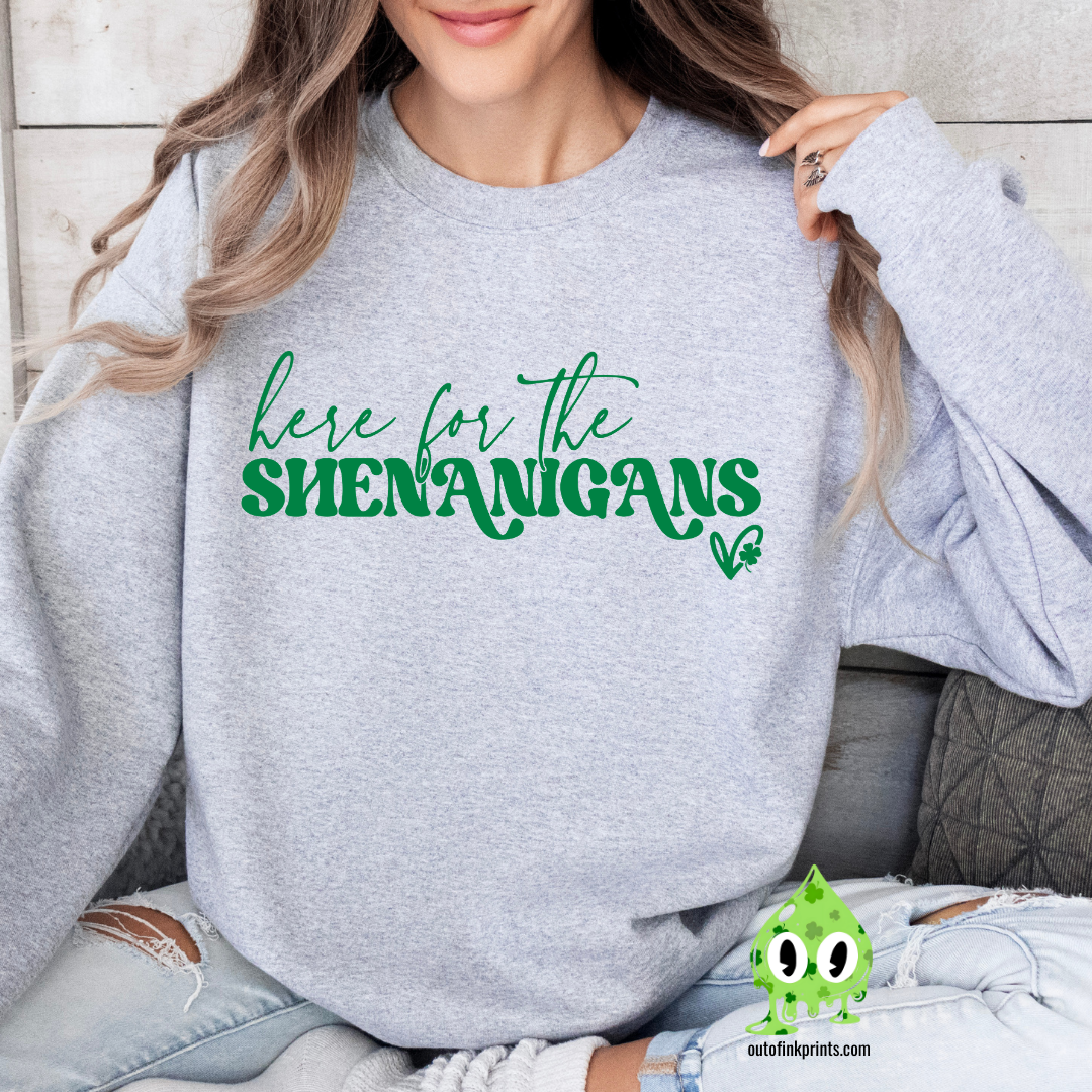 A woman wearing a grey sweatshirt with the text 'here for the SHENANIGANS' printed on it.