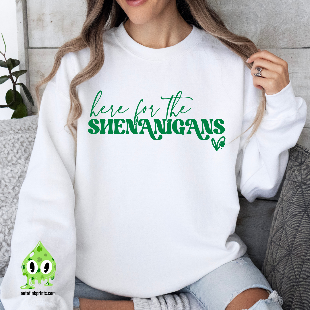 A woman wearing a white sweatshirt with the text 'here for the SHENANIGANS' printed on it.