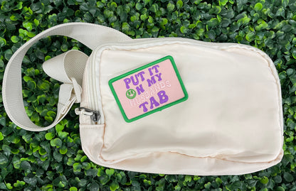  an embroidered patch with the text 'PUT IT ON MY HUSBAND'S TAB' on a green background and a white fanny pack
