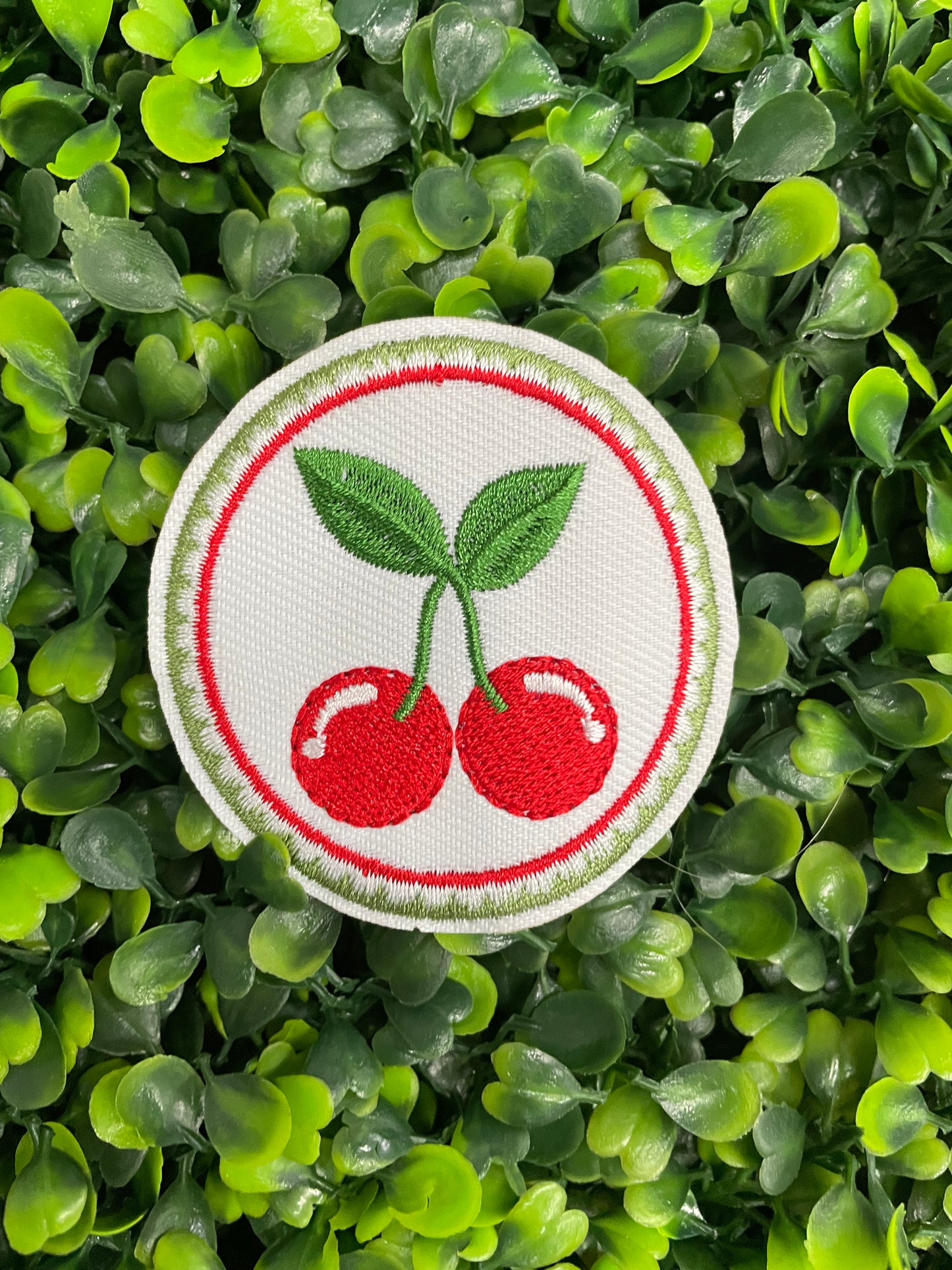 A round embroidered patch with two red cherries and green leaves on a white background