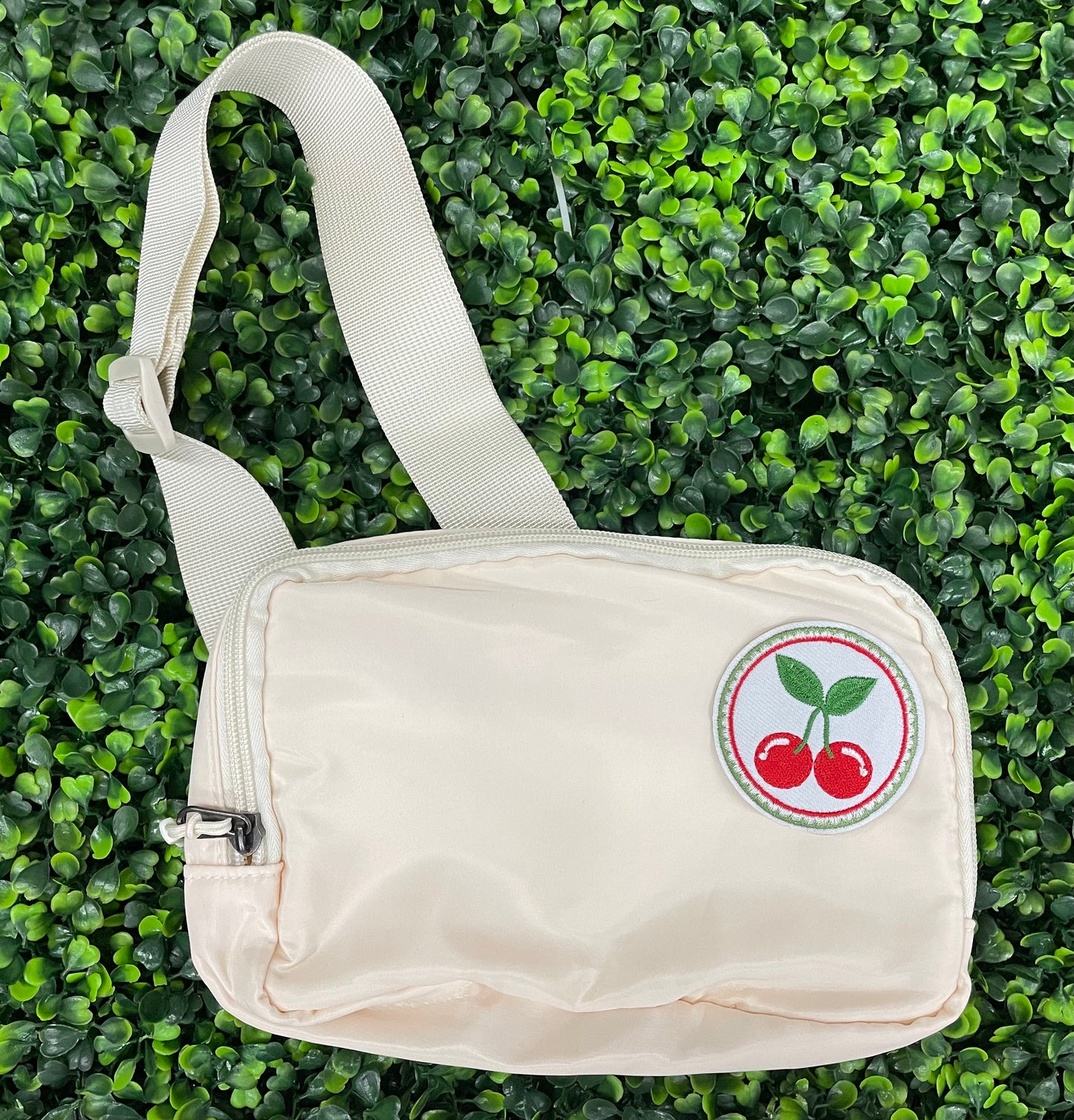A round embroidered patch with two red cherries and green leaves on a white background, on a white fanny pack