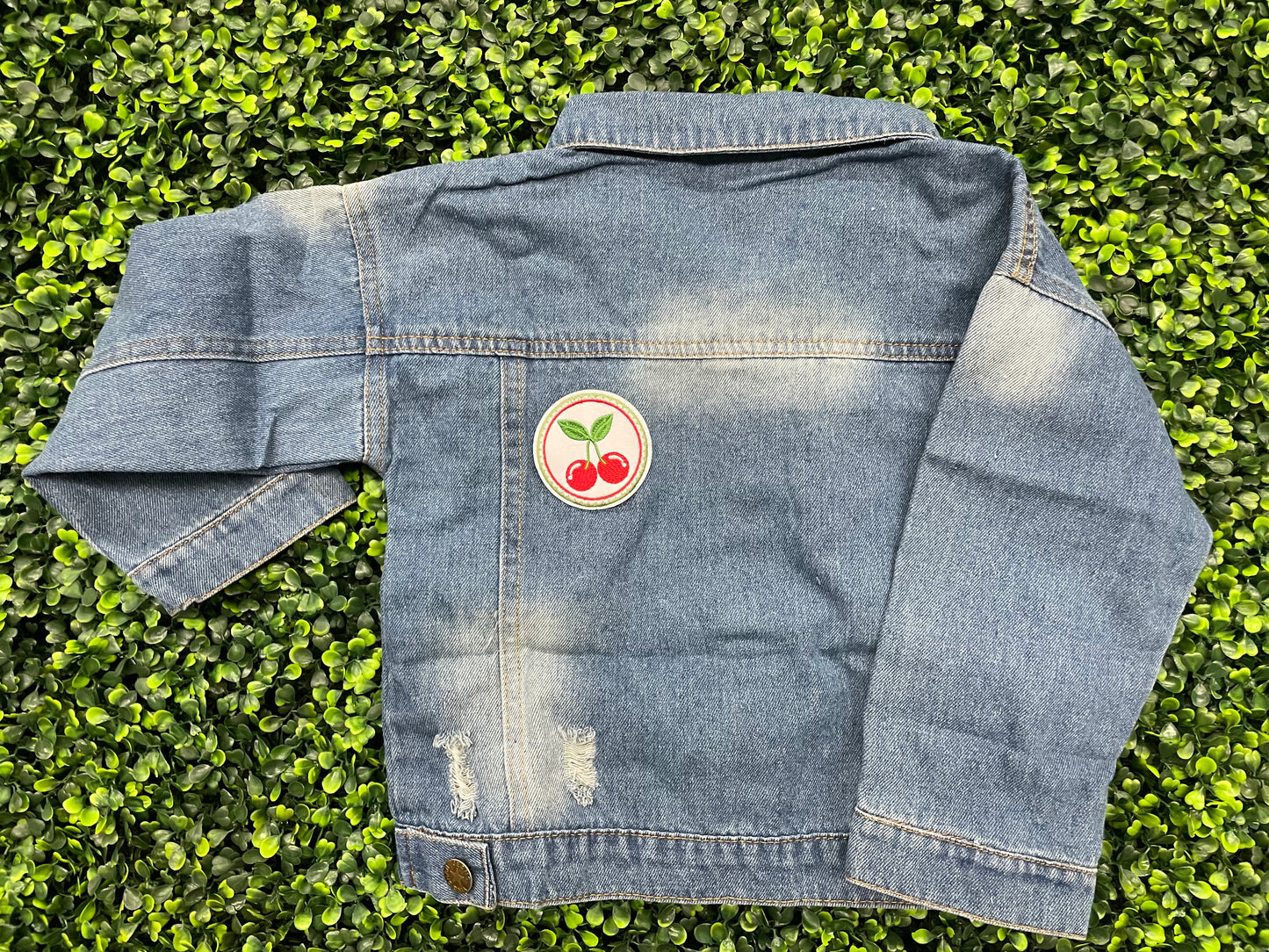 A round embroidered patch with two red cherries and green leaves on a white background, on a jean jacket
