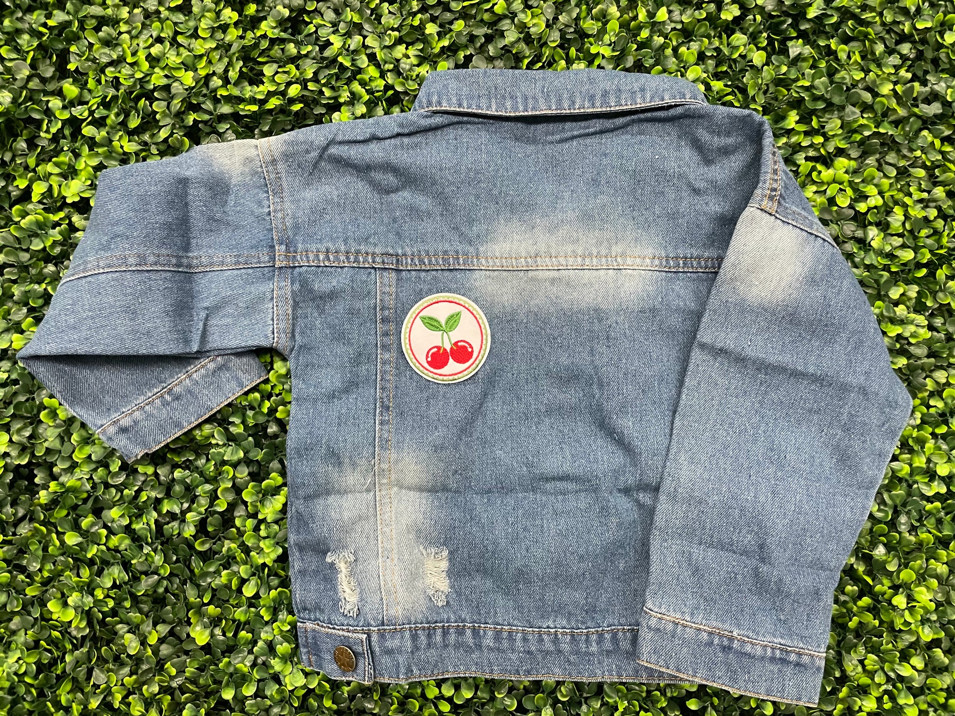 A round embroidered patch with two red cherries and green leaves on a white background, on a jean jacket