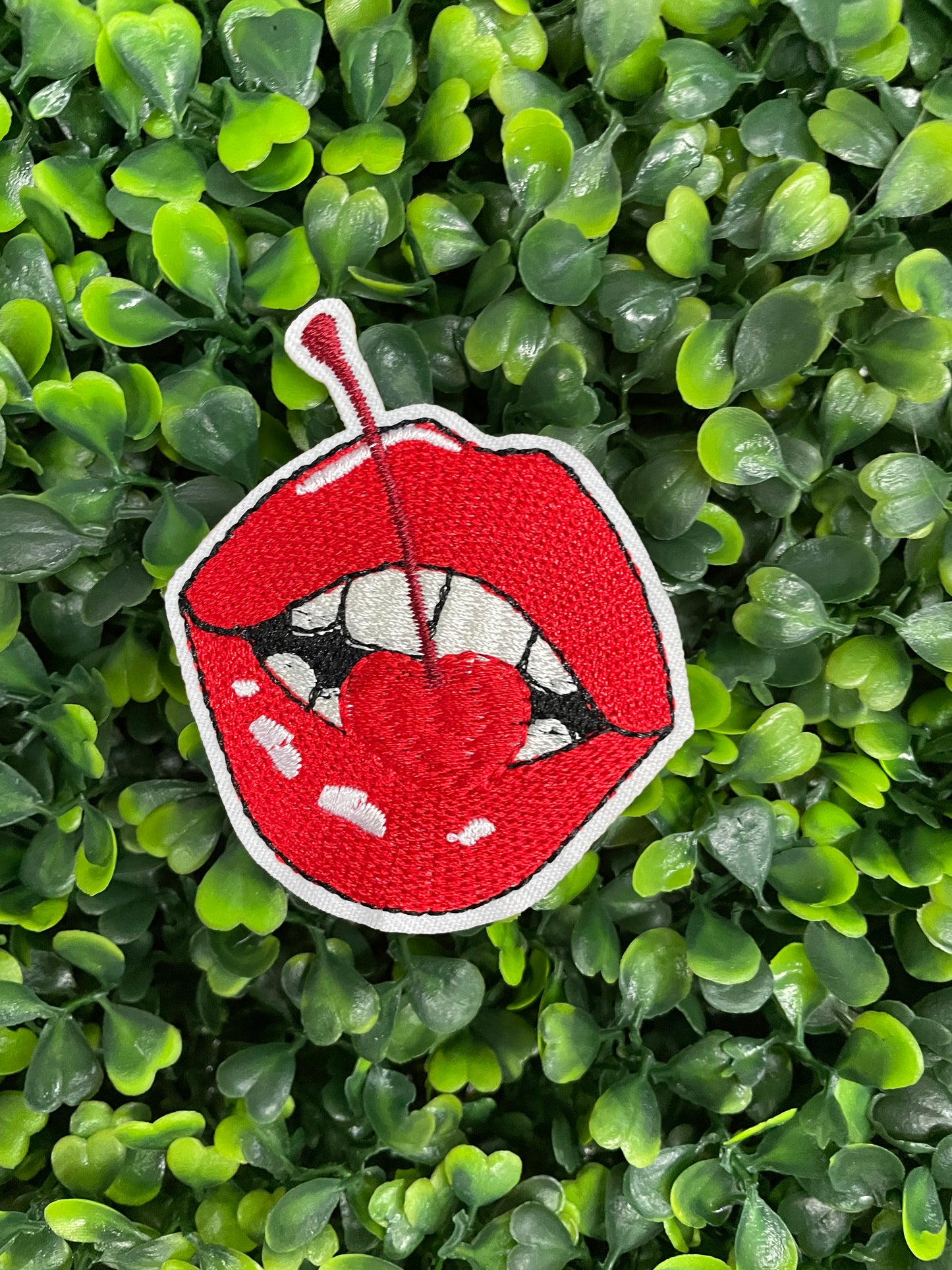  red lips embroidered patch with a cherry, with greenery in the background.