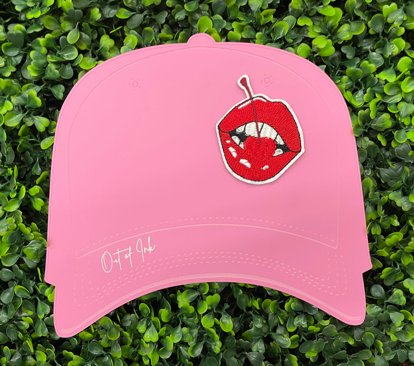 pink hat template with a red lips embroidered patch with a cherry, with greenery in the background.