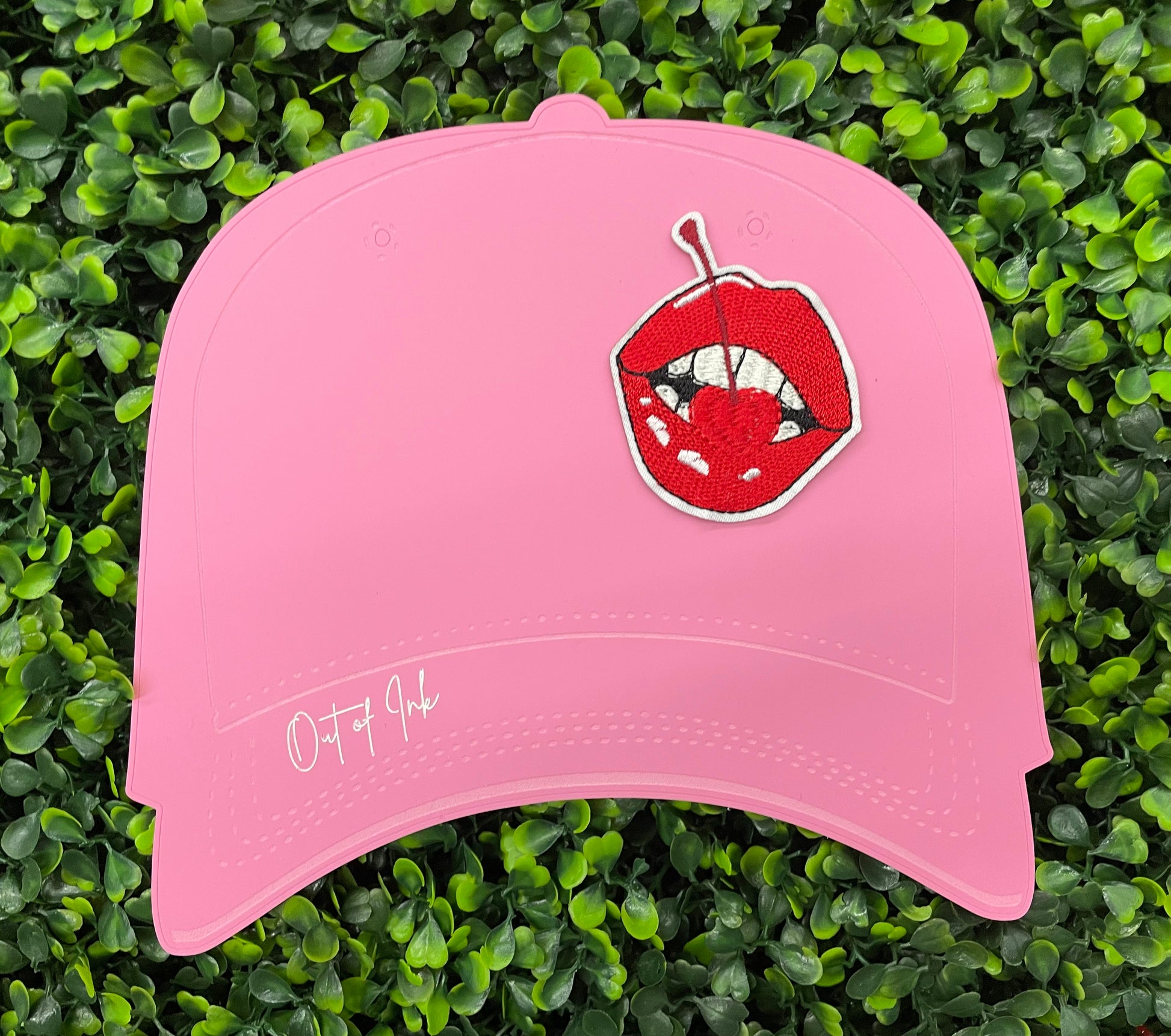 pink hat template with a red lips embroidered patch with a cherry, with greenery in the background.