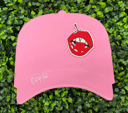pink hat template with a red lips embroidered patch with a cherry, with greenery in the background.