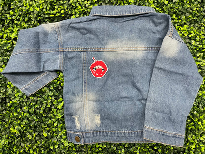 Jean jacket with  a red lips embroidered patch with a cherry, with greenery in the background.