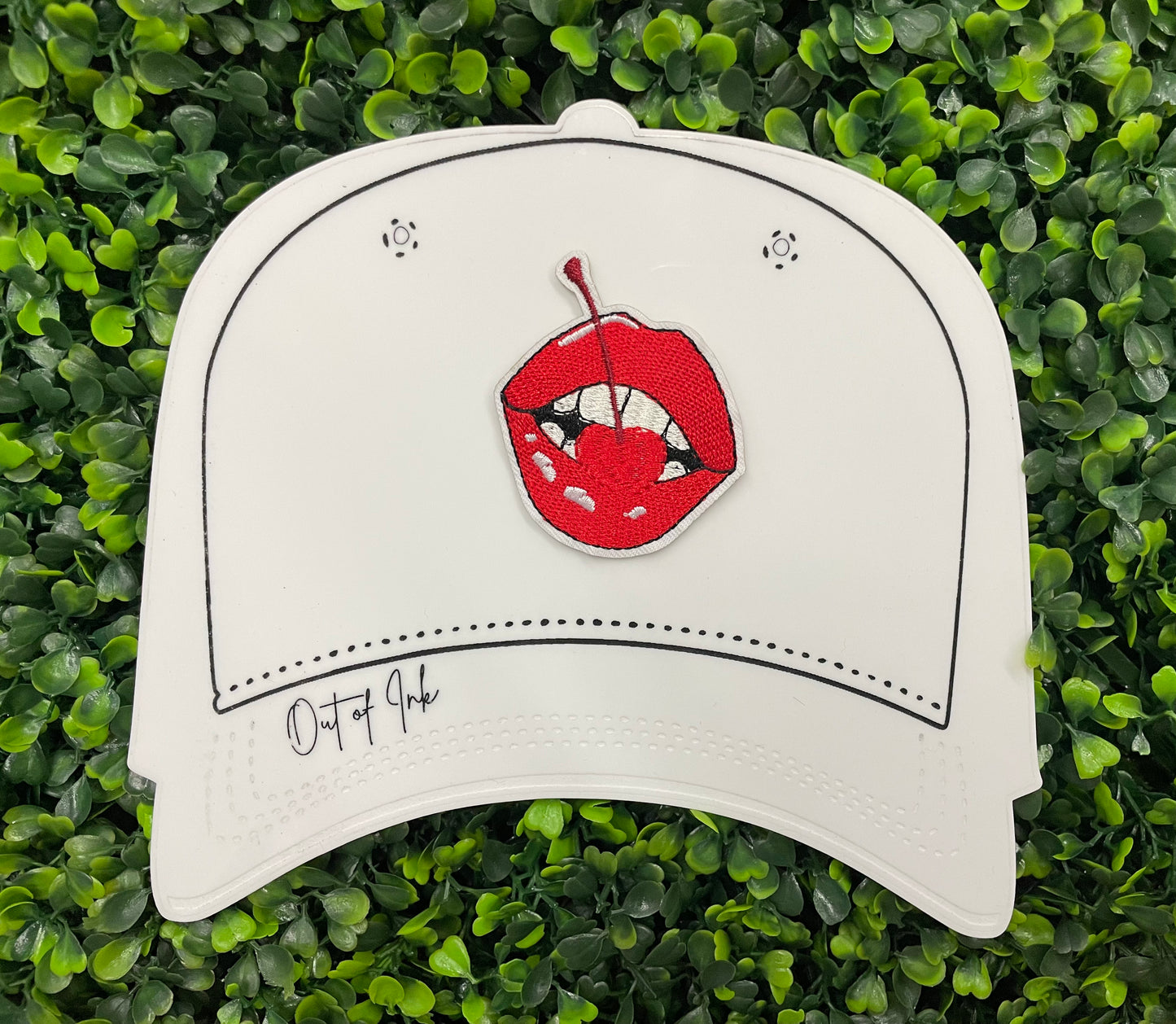 white hat template with a red lips embroidered patch with a cherry, with greenery in the background.