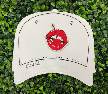 white hat template with a red lips embroidered patch with a cherry, with greenery in the background.