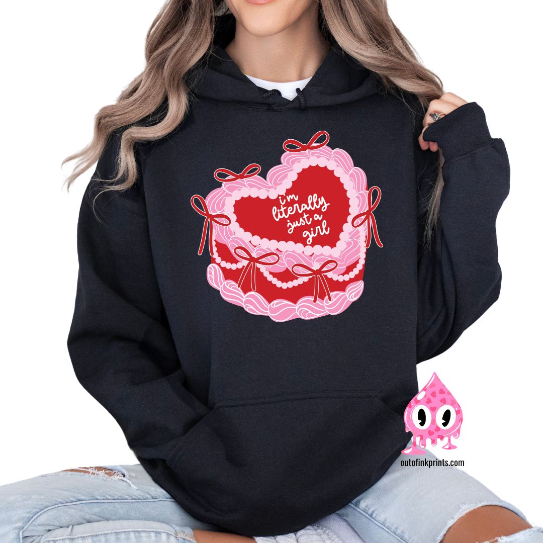 A woman wearing a black hoodie with a heart and a cake design, featuring the text 'I'm Literally Just a Girl'.
