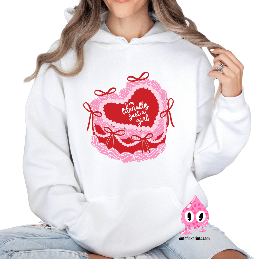 A woman wearing a white hoodie with a heart and a cake design, featuring the text 'I'm Literally Just a Girl'.