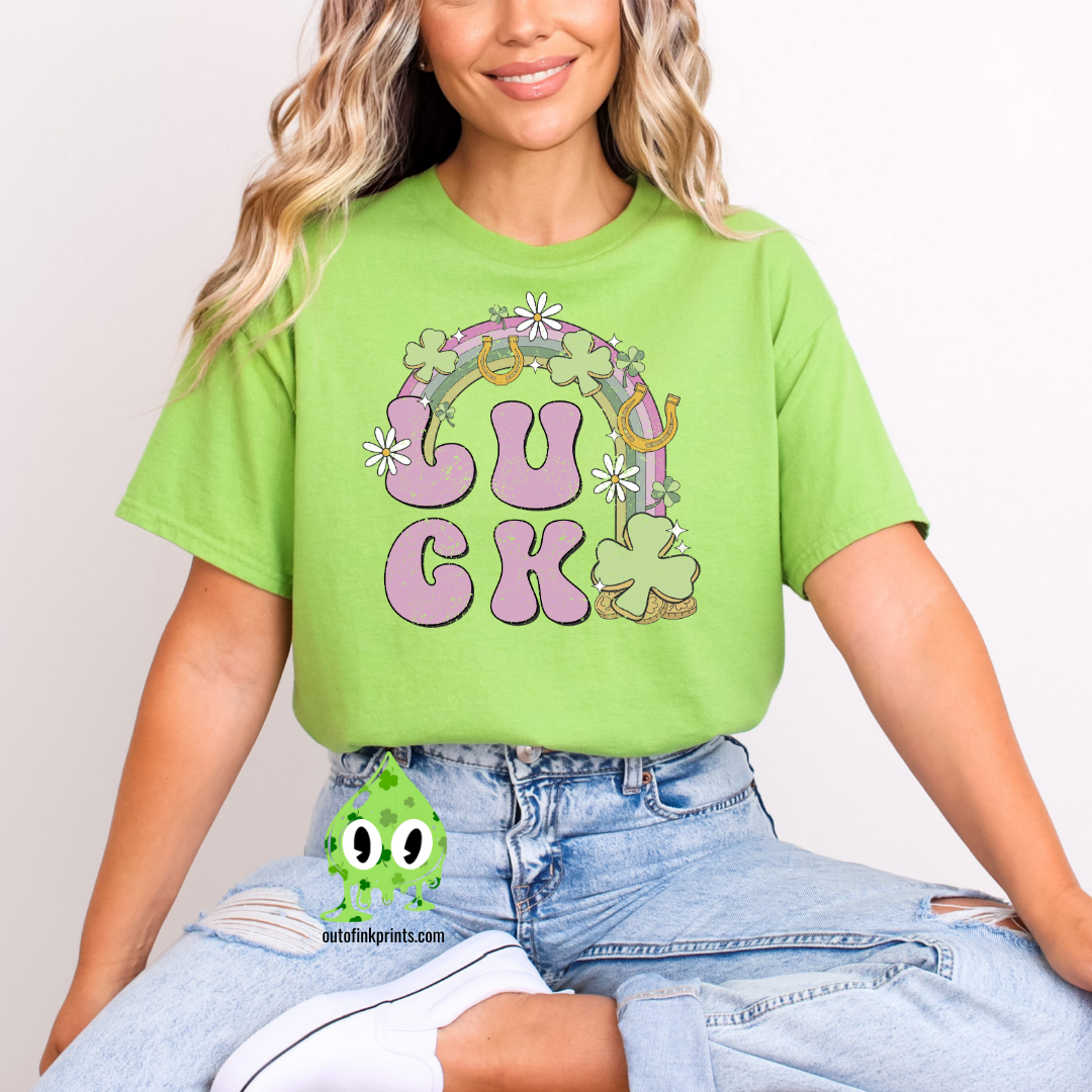 A person wearing a green 'LUCK Rainbow' T-shirt with a checkered pattern and decorative elements such as a four leaf clover and smiley faces.