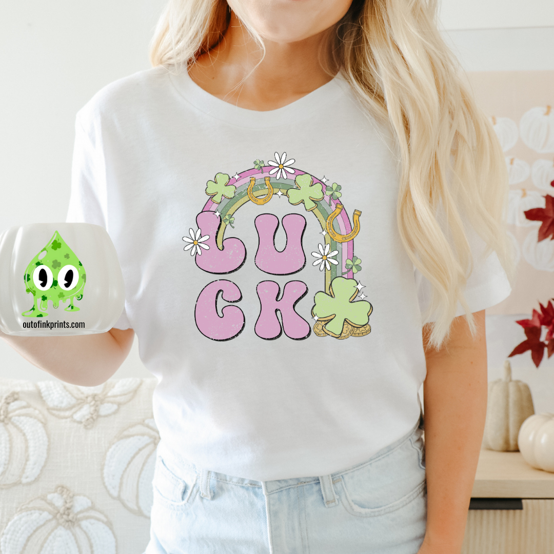 A person wearing a white 'LUCK Rainbow' T-shirt with a checkered pattern and decorative elements such as a four leaf clover and smiley faces.