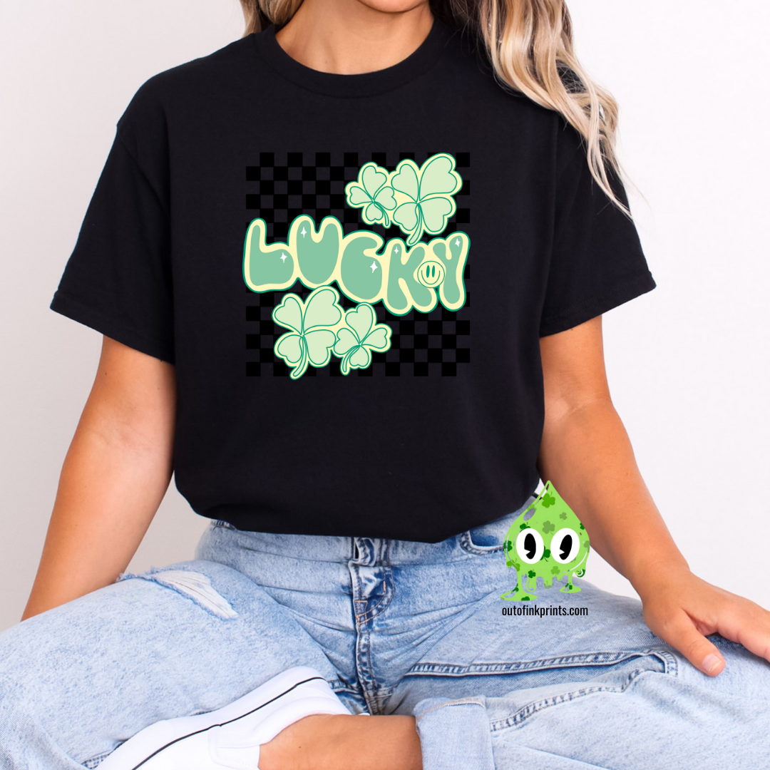 A person wearing a black  'Lucky Checkered' T-shirt with a checkered pattern and green shamrock graphics, accompanied by the text 'LUCKY!' displayed prominently.