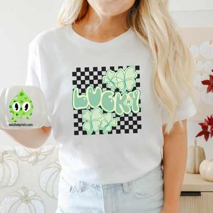 A person wearing a white 'Lucky Checkered' T-shirt with a checkered pattern and green shamrock graphics, accompanied by the text 'LUCKY!' displayed prominently.